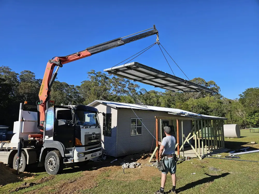 Crane truck lifting a roof frame beside a house under construction