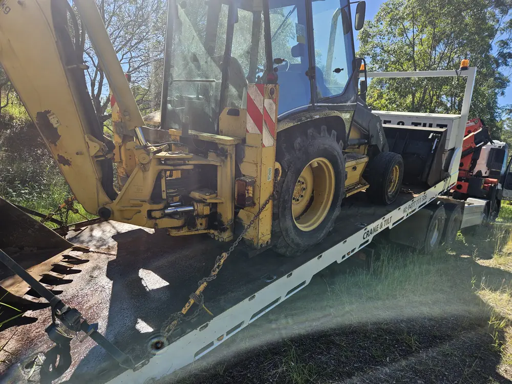 Backhoe loader secured on a tilt tray, showing the wheels and loading deck
