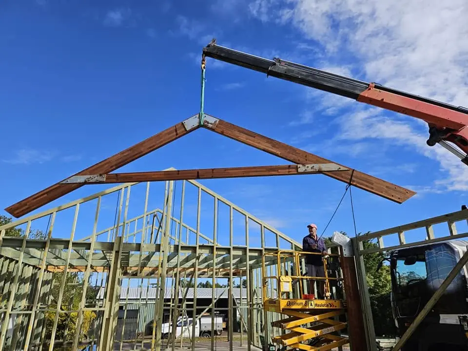 Crane truck lifting roof framing above a timber-framed building