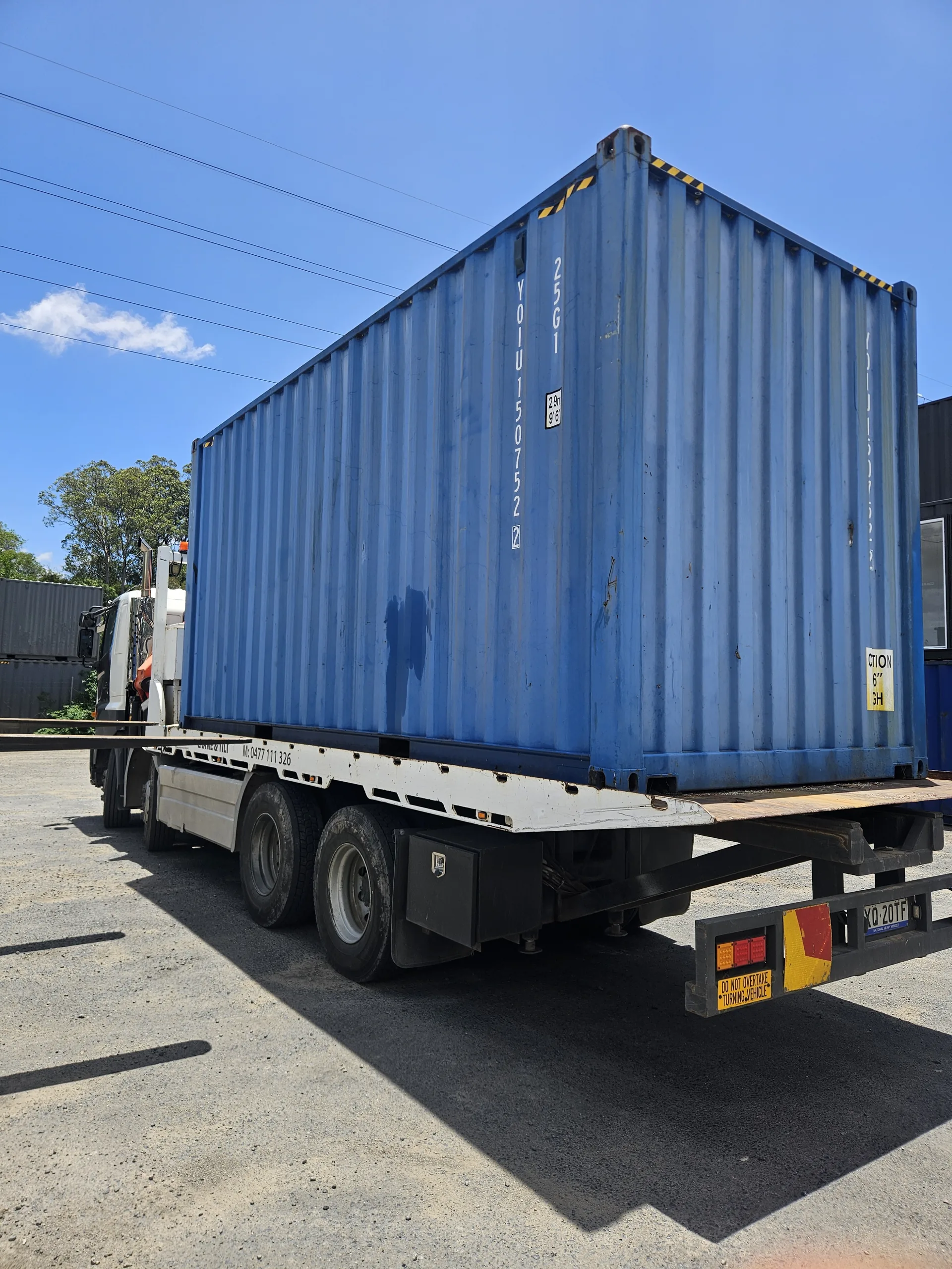 Blue shipping container loaded onto the tilt tray truck