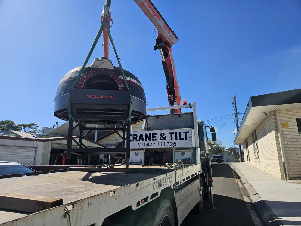 Crane truck lifting a large spa or pod-shaped load from the tray