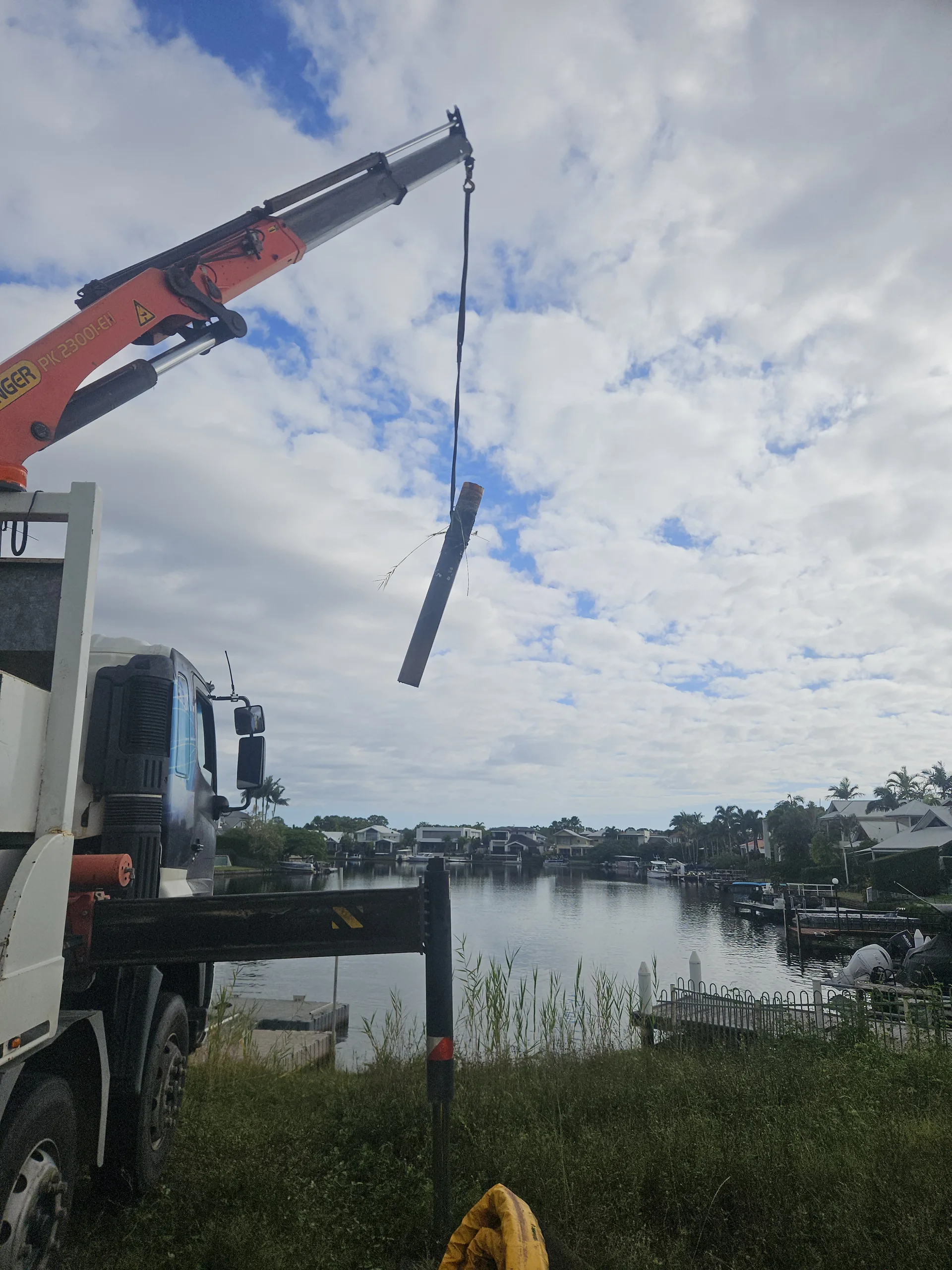 Crane truck lifting a long narrow load beside the waterfront
